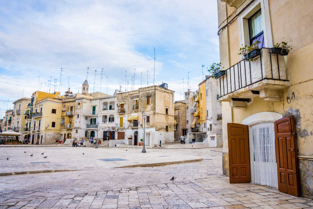 Spacious town square in Bari, Italy, surrounded by historic buildings with balconies and a clear blue sky overhead